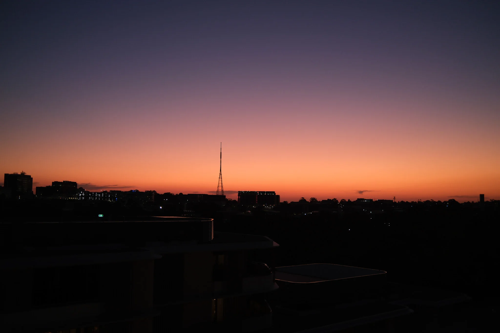 The city skyline is silhouetted against a vibrant gradient of purple and orange. Distant building lights illuminate the dark urban landscape.